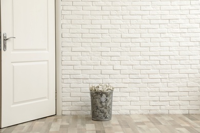 Photo of Metal bin with crumpled paper on floor against brick wall, space for text