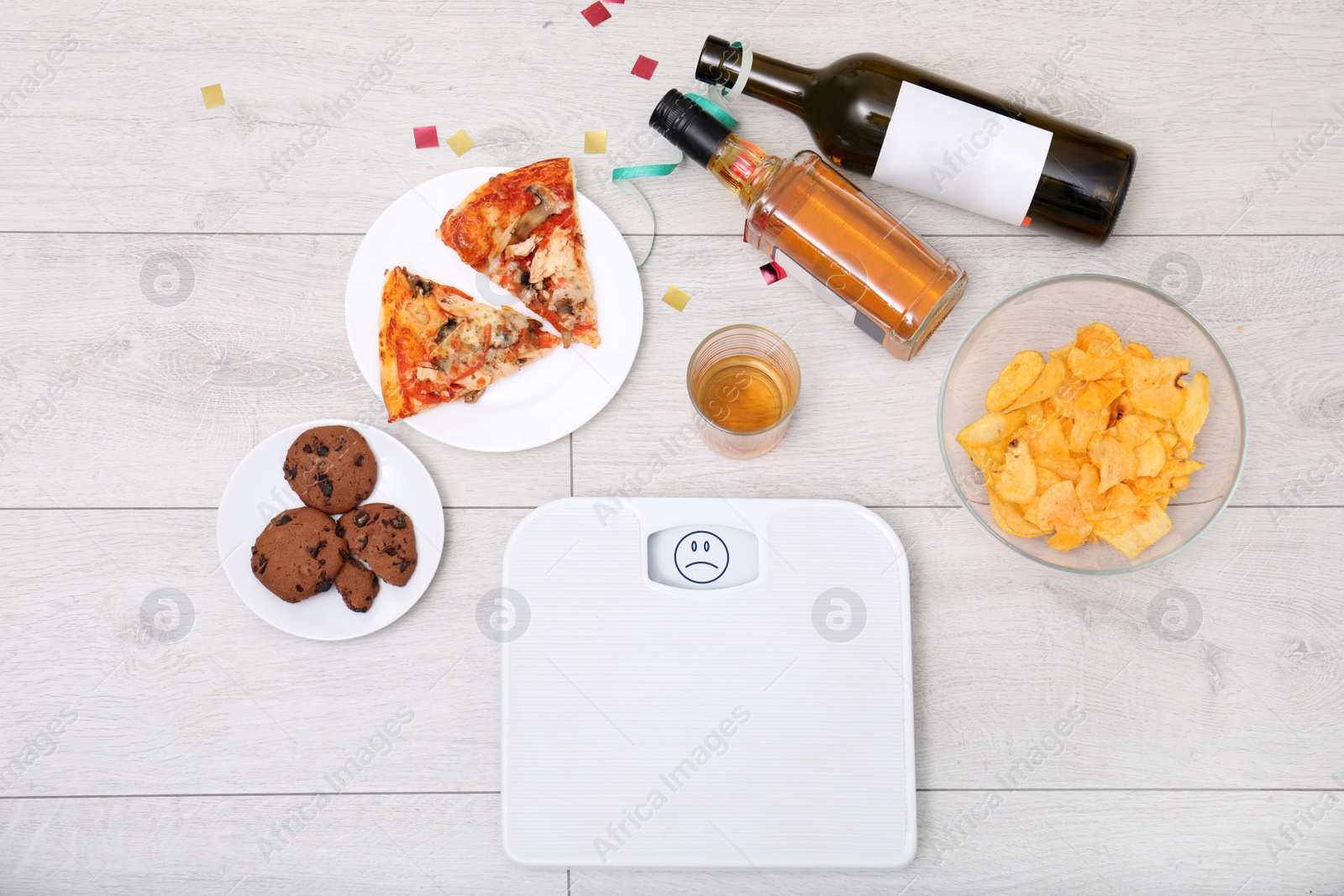 Photo of Digital scales, junk food and alcohol on wooden floor after party, top view