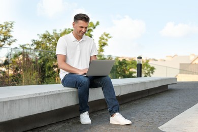 Photo of Handsome man using laptop on stone bench outdoors