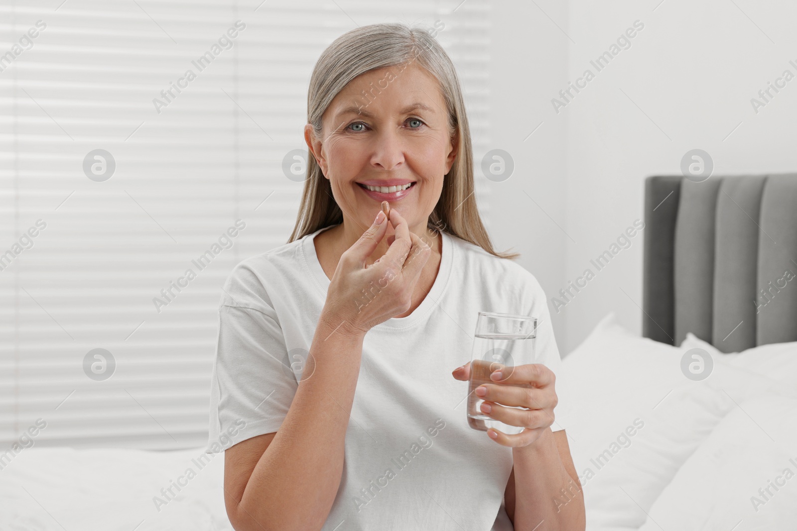 Photo of Beautiful woman taking vitamin pill in bedroom