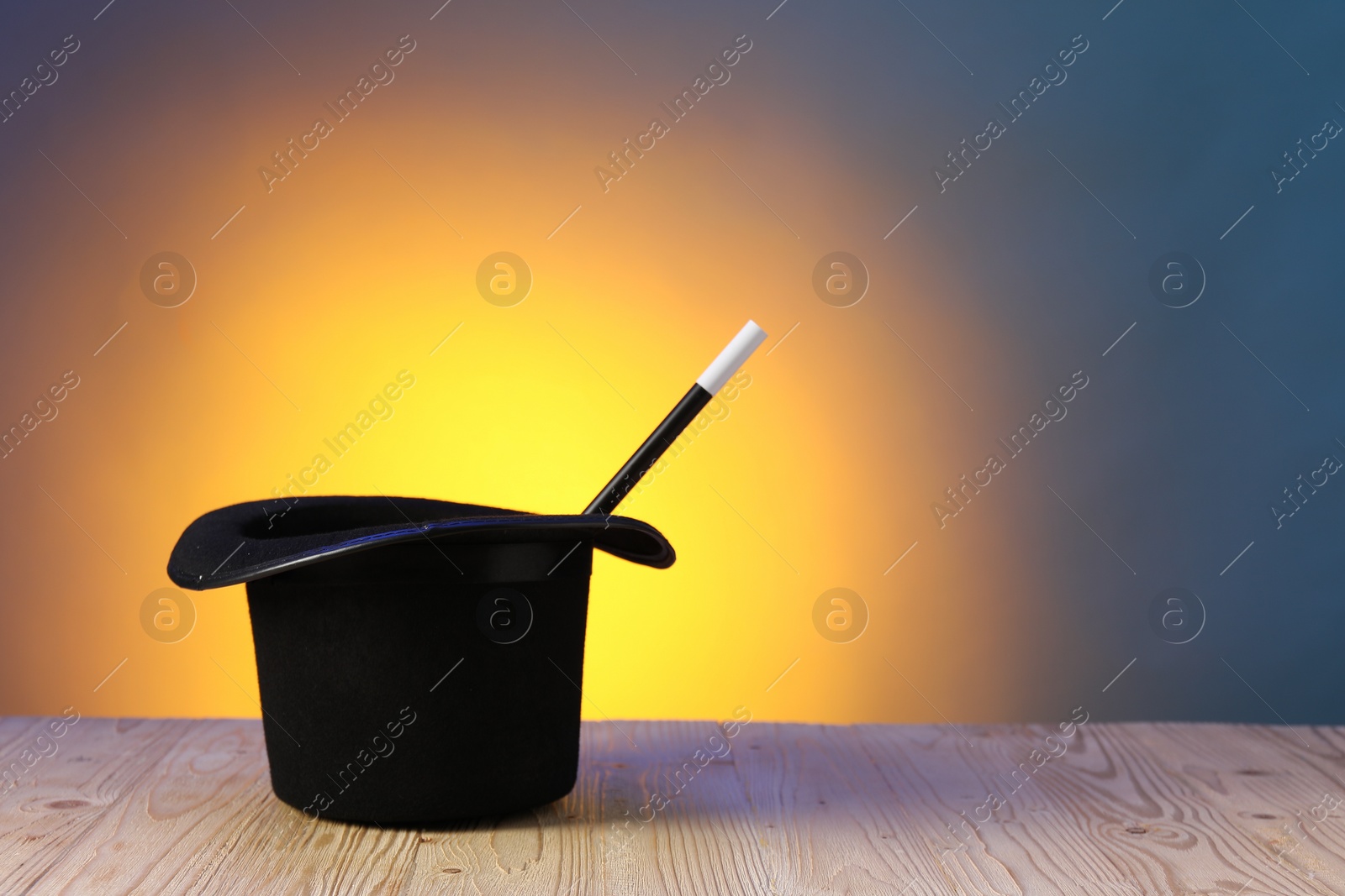 Photo of Magician's hat and wand on wooden table against color background, space for text