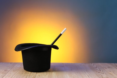 Photo of Magician's hat and wand on wooden table against color background, space for text