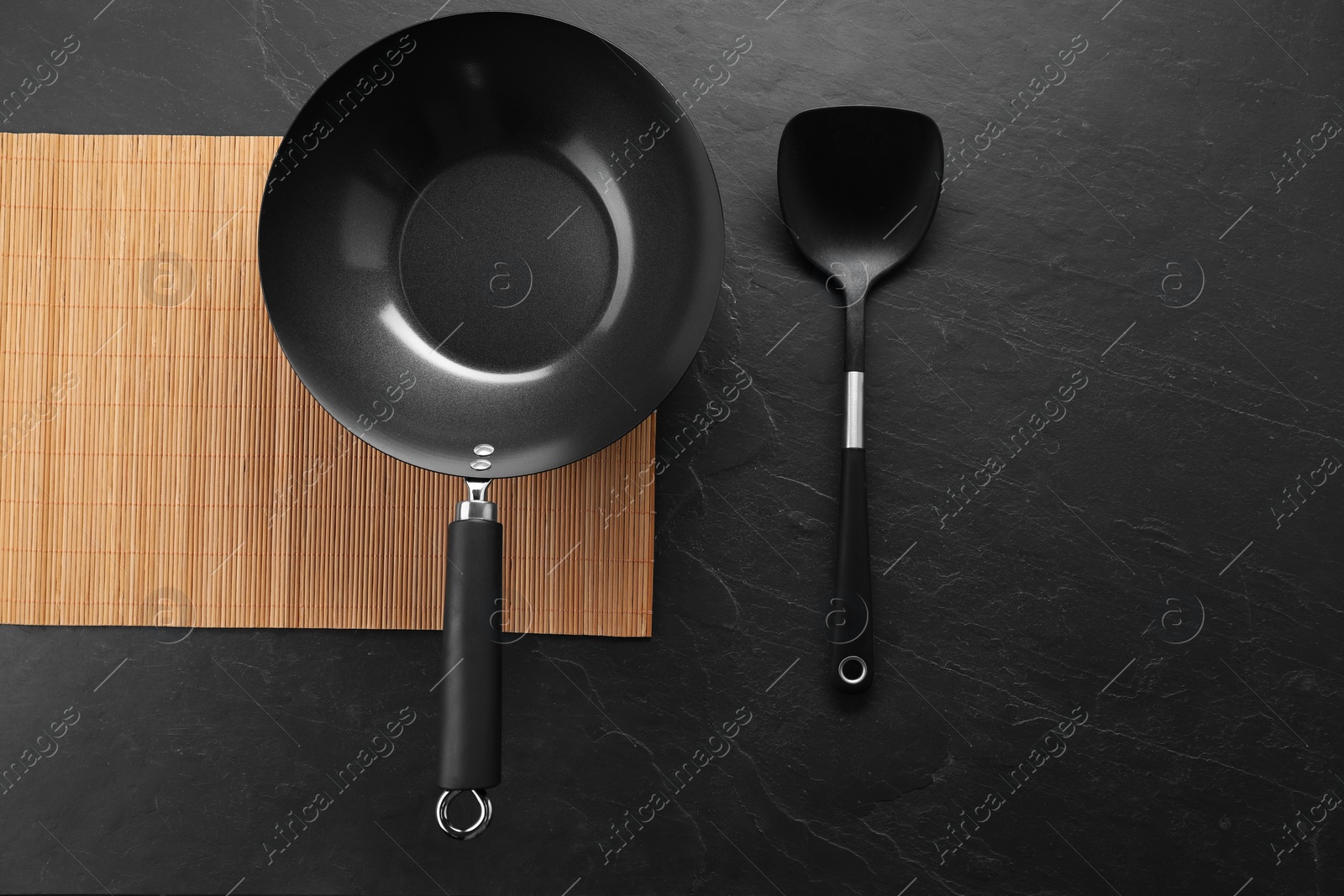 Photo of Black metal wok and spatula on dark textured table, top view