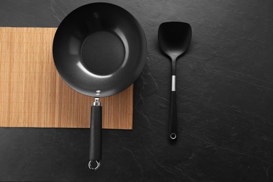 Black metal wok and spatula on dark textured table, top view