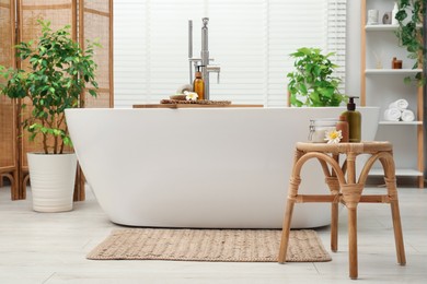 Stylish bathroom interior with ceramic tub, spa products and green houseplants