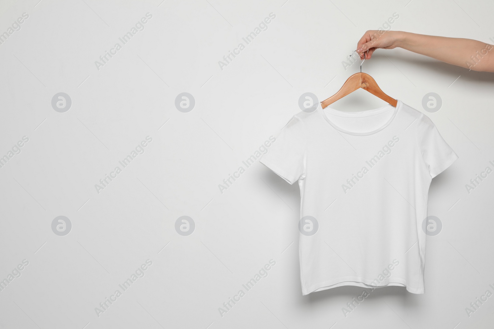 Photo of Woman holding hanger with blank t-shirt on white background. Mock up for design