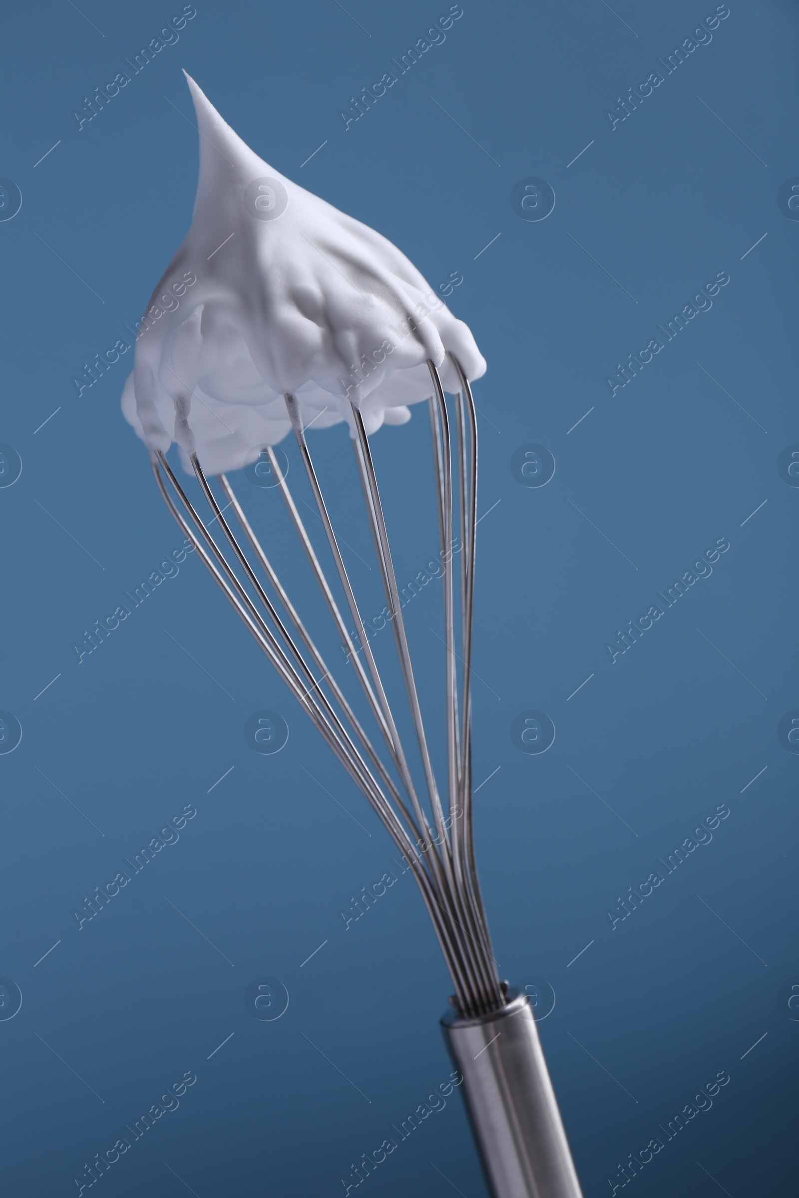 Photo of Whisk with whipped cream on light blue background