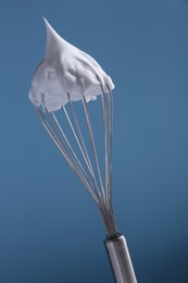 Whisk with whipped cream on light blue background