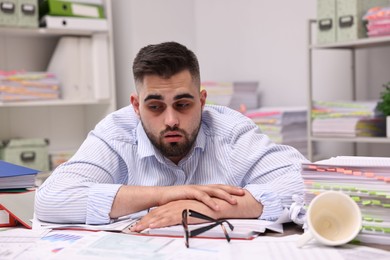 Overwhelmed man surrounded by documents at workplace in office