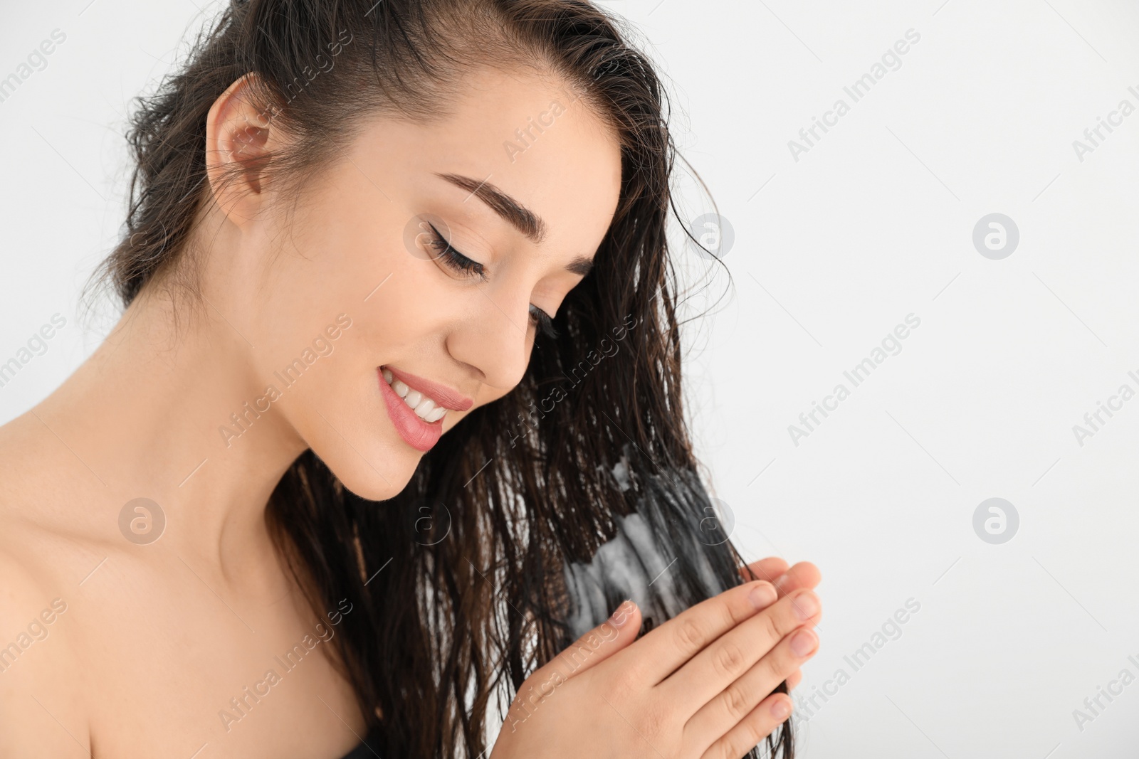 Photo of Beautiful young woman applying hair conditioner against white background. Space for text