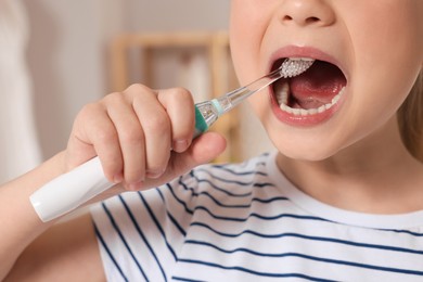 Photo of Little girl brushing her teeth with electric toothbrush indoors, closeup