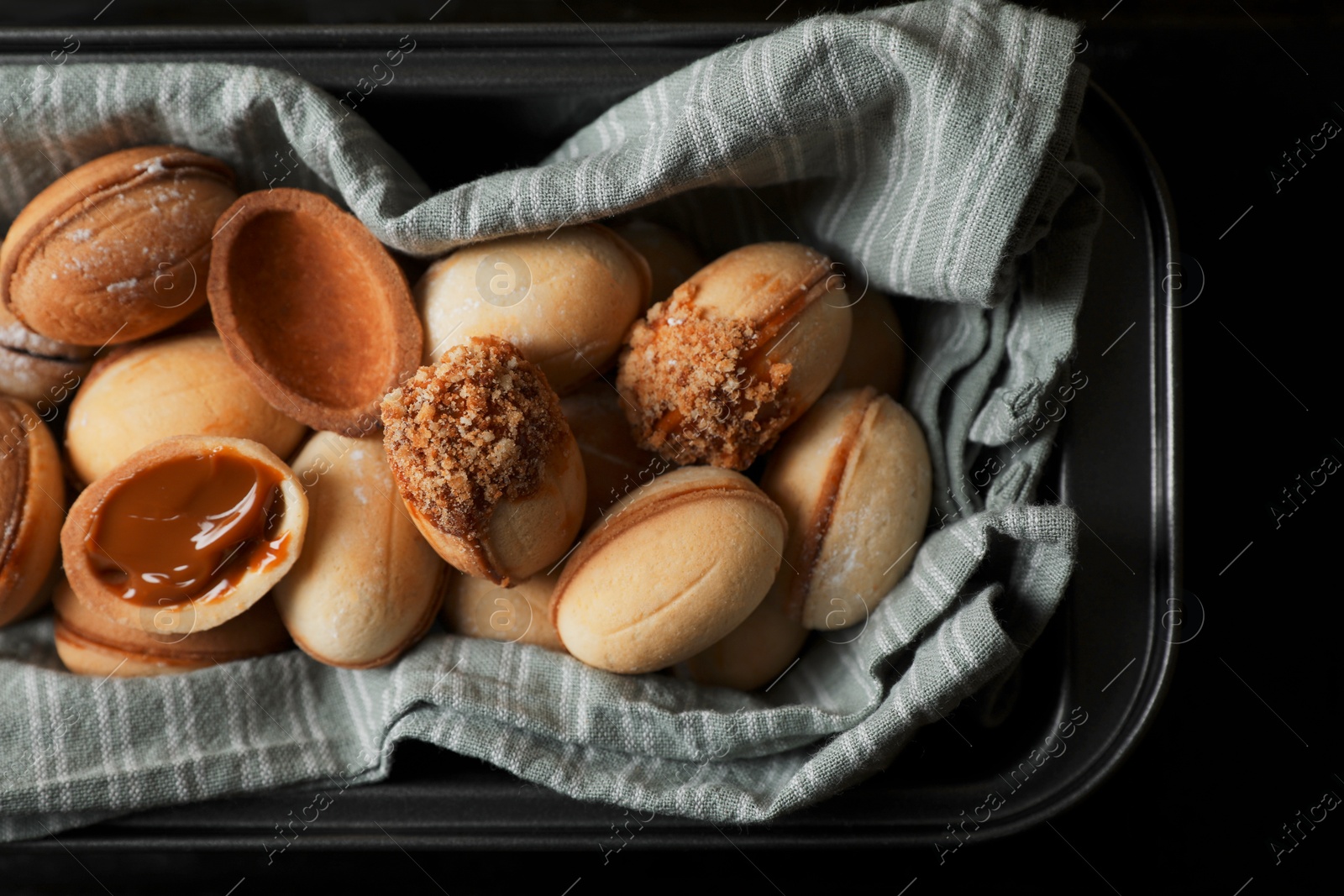 Photo of Freshly baked homemade walnut shaped cookies with condensed milk on black table, top view