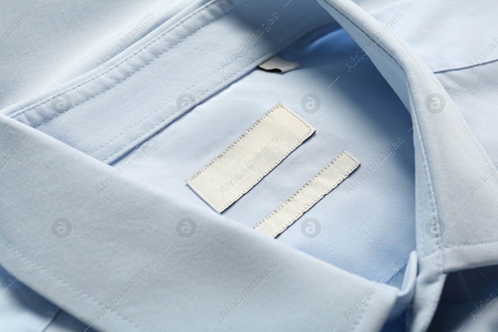 Photo of Blank clothing labels on light blue shirt, closeup