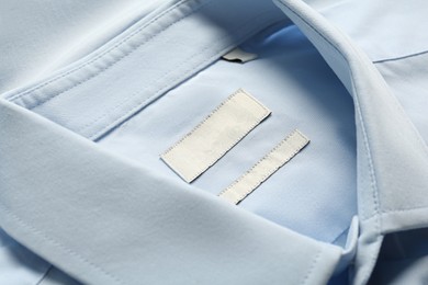 Photo of Blank clothing labels on light blue shirt, closeup