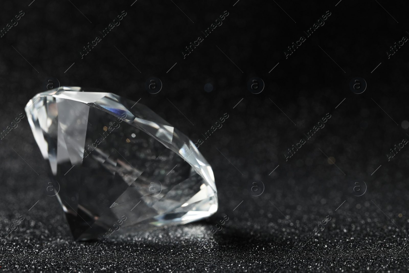Photo of Beautiful dazzling diamond on shiny glitter background, closeup. Space for text