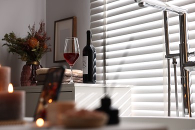 Bottle of wine, towels and flowers on chest of drawers in bathroom, selective focus