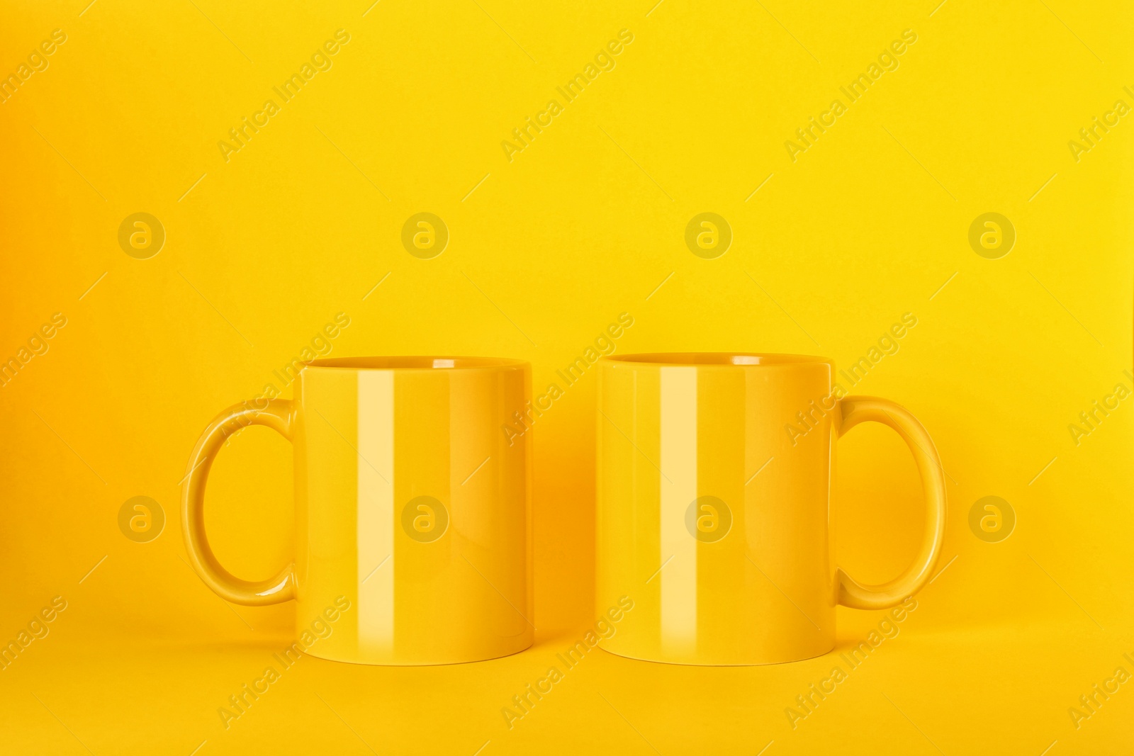 Two blank ceramic mugs on yellow background Photo of Two blank ceramic mugs on yellow background