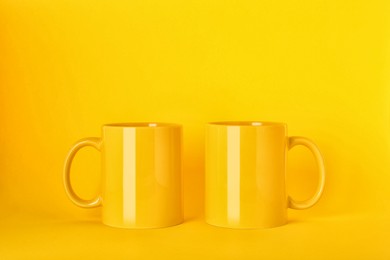 Photo of Two blank ceramic mugs on yellow background