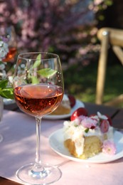 Vase with spring flowers, wine and cake on table served for romantic date in garden