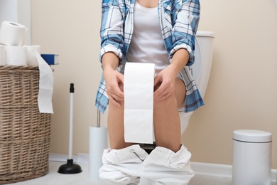Woman with paper roll sitting on toilet bowl in bathroom