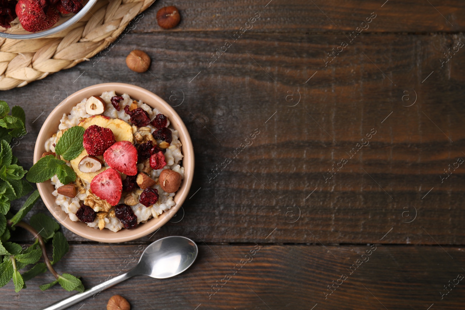 Photo of Oatmeal with freeze dried fruits, nuts and mint on wooden table, flat lay. Space for text