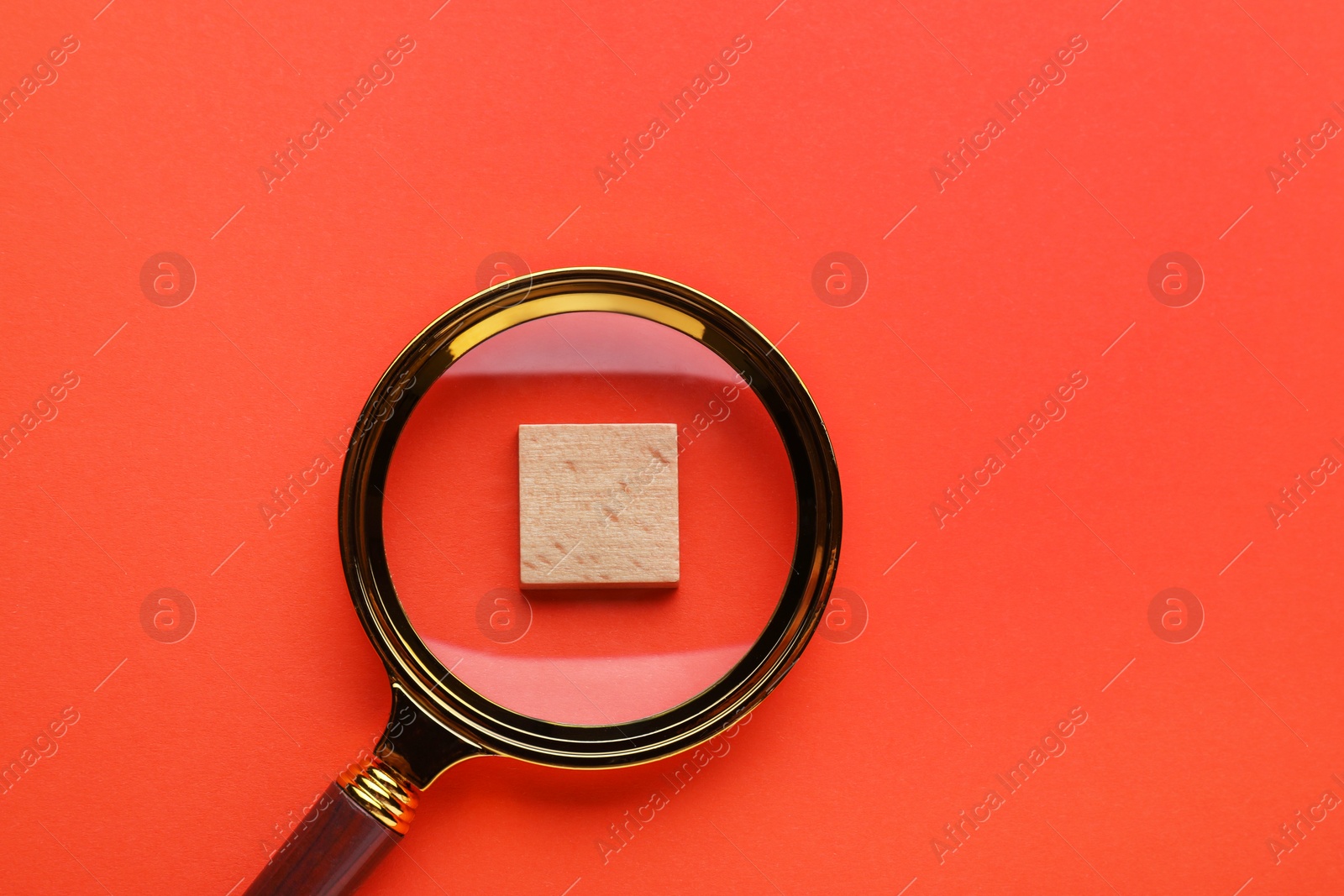 Photo of Looking at wooden cube through magnifying glass on red background, top view