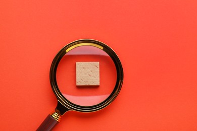 Looking at wooden cube through magnifying glass on red background, top view