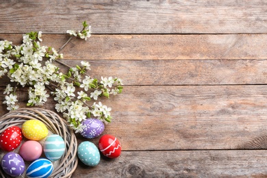 Photo of Flat lay composition with painted Easter eggs and blossoming branches on wooden background. Space for text