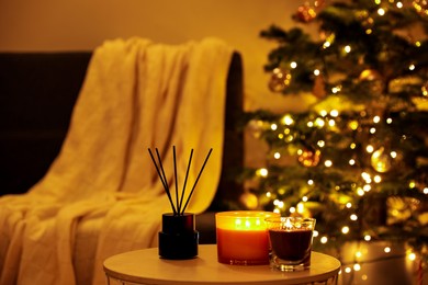 Beautiful candles and reed air freshener near Christmas tree indoors. Cosy atmosphere