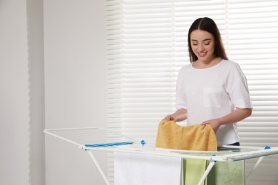 Photo of Woman hanging clean terry towels on drying rack indoors