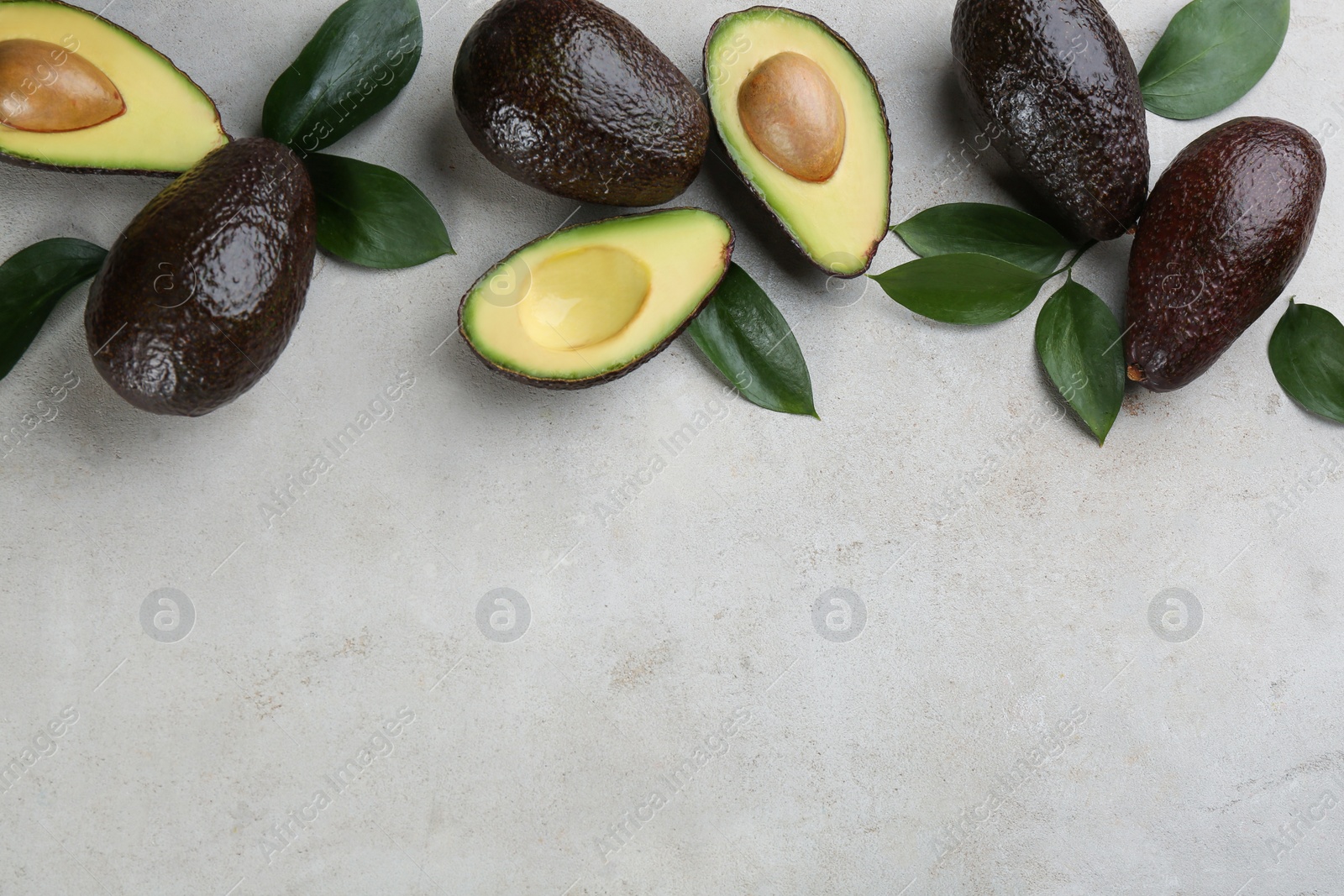 Photo of Whole and cut avocados with green leaves on light table, flat lay. Space for text