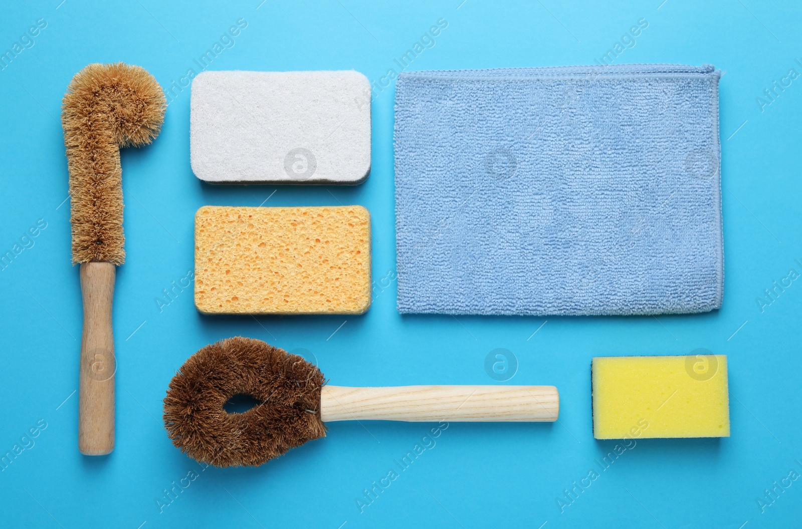 Photo of Many different sponges and other cleaning products on light blue background, flat lay