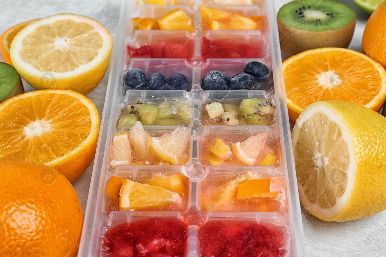 Photo of Ice cubes with fruits and berries in tray near ingredients on light table