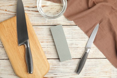 Photo of Sharpening stone, knives and water on white wooden table, flat lay
