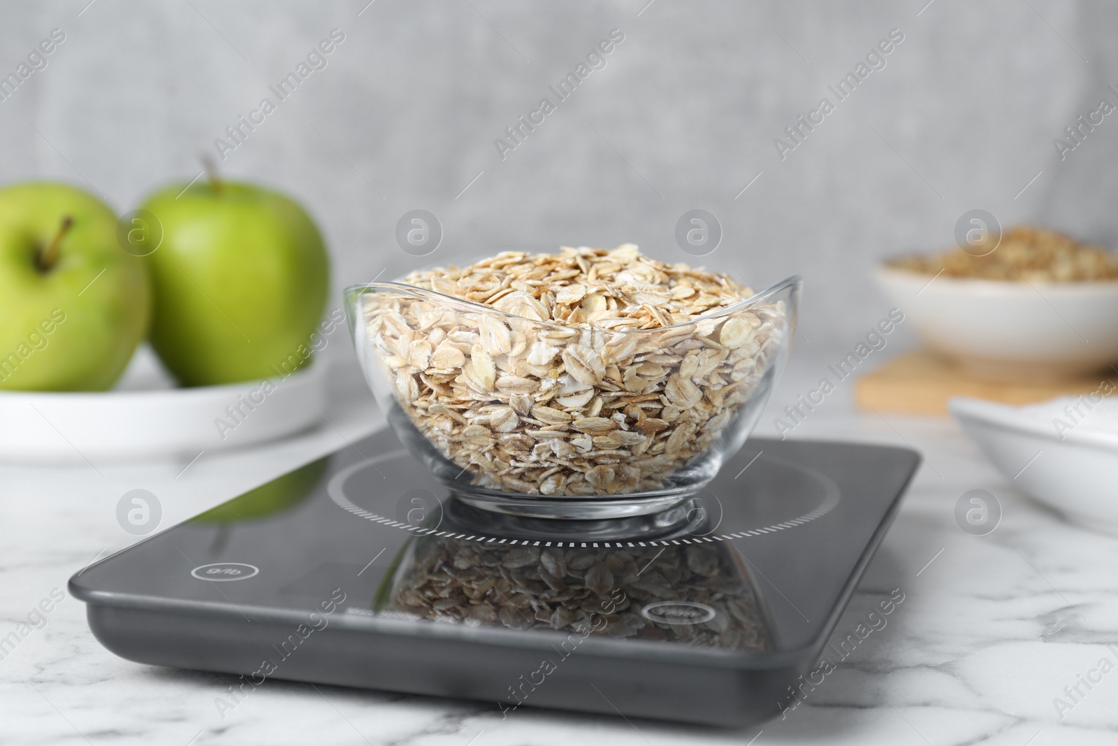 Photo of Digital kitchen scale with oat flakes on white marble table