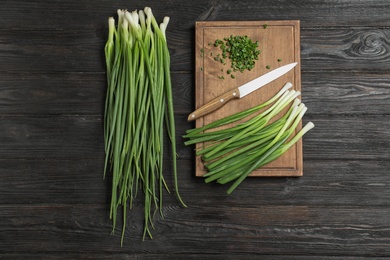 Photo of Flat lay composition with green onions, knife and board on dark wooden table