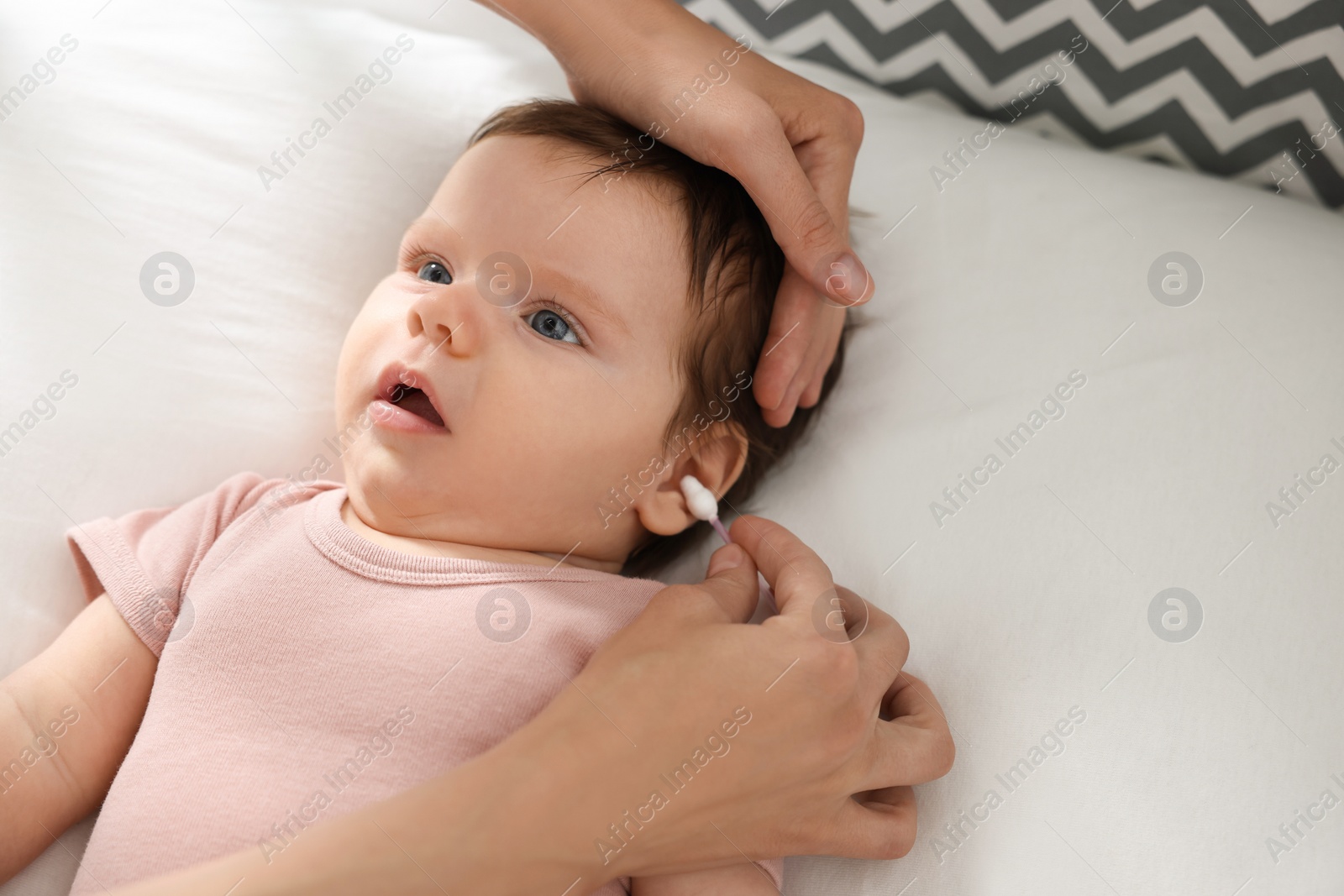 Photo of Mother cleaning ears of her baby with cotton bud on bed, closeup