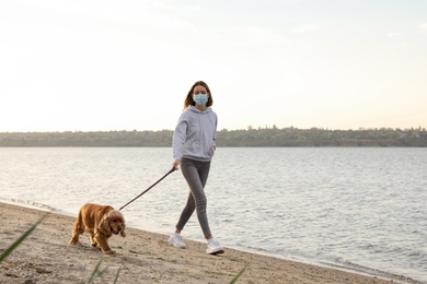 Photo of Woman in protective mask with English Cocker Spaniel on beach. Walking dog during COVID-19 pandemic
