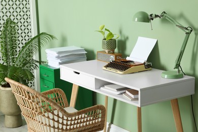 Photo of Writer's workplace with typewriter on wooden desk near pale green wall in room