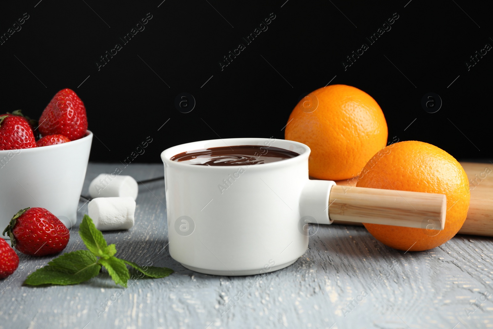 Photo of Fondue pot with chocolate, fruits and marshmallow on grey wooden table