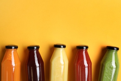 Bottles with delicious colorful juices on yellow background, flat lay. Space for text