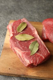 Photo of Piece of raw beef meat with bay leaves on grey table, closeup
