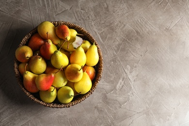 Photo of Wicker bowl with ripe pears on grey background, top view. Space for text