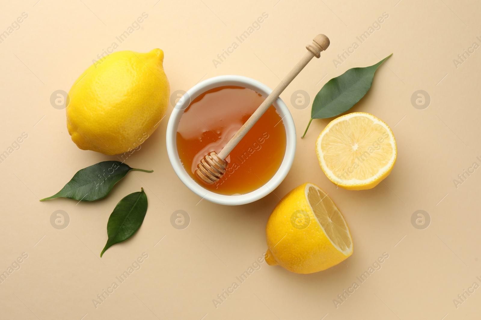 Photo of Ripe lemons, leaves, bowl of honey and dipper on beige background, flat lay