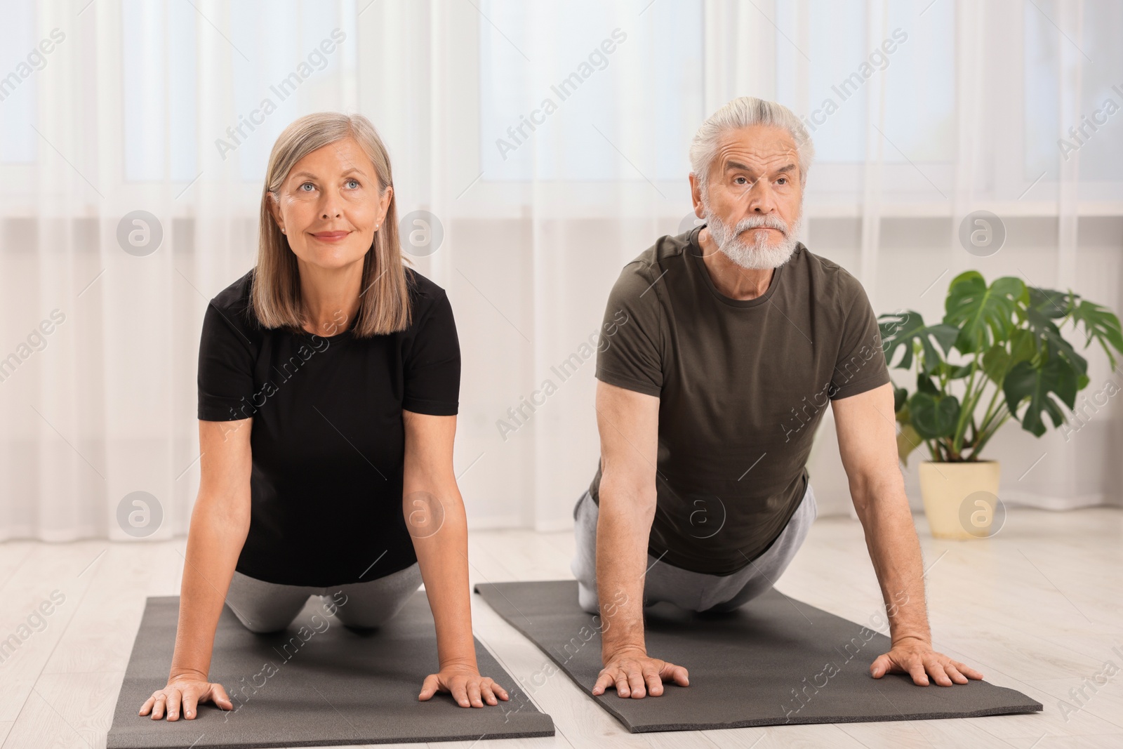 Photo of Senior couple practicing yoga on mats at home