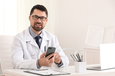 Photo of Male doctor with smartphone at table in office