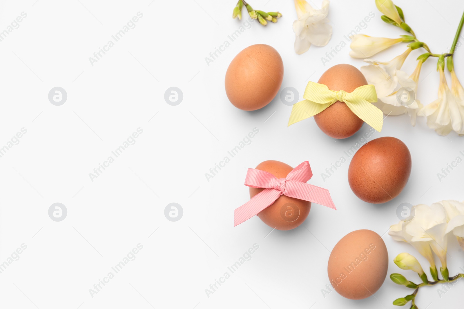 Photo of Easter eggs with colorful bows and flowers on white background, flat lay. Space for text