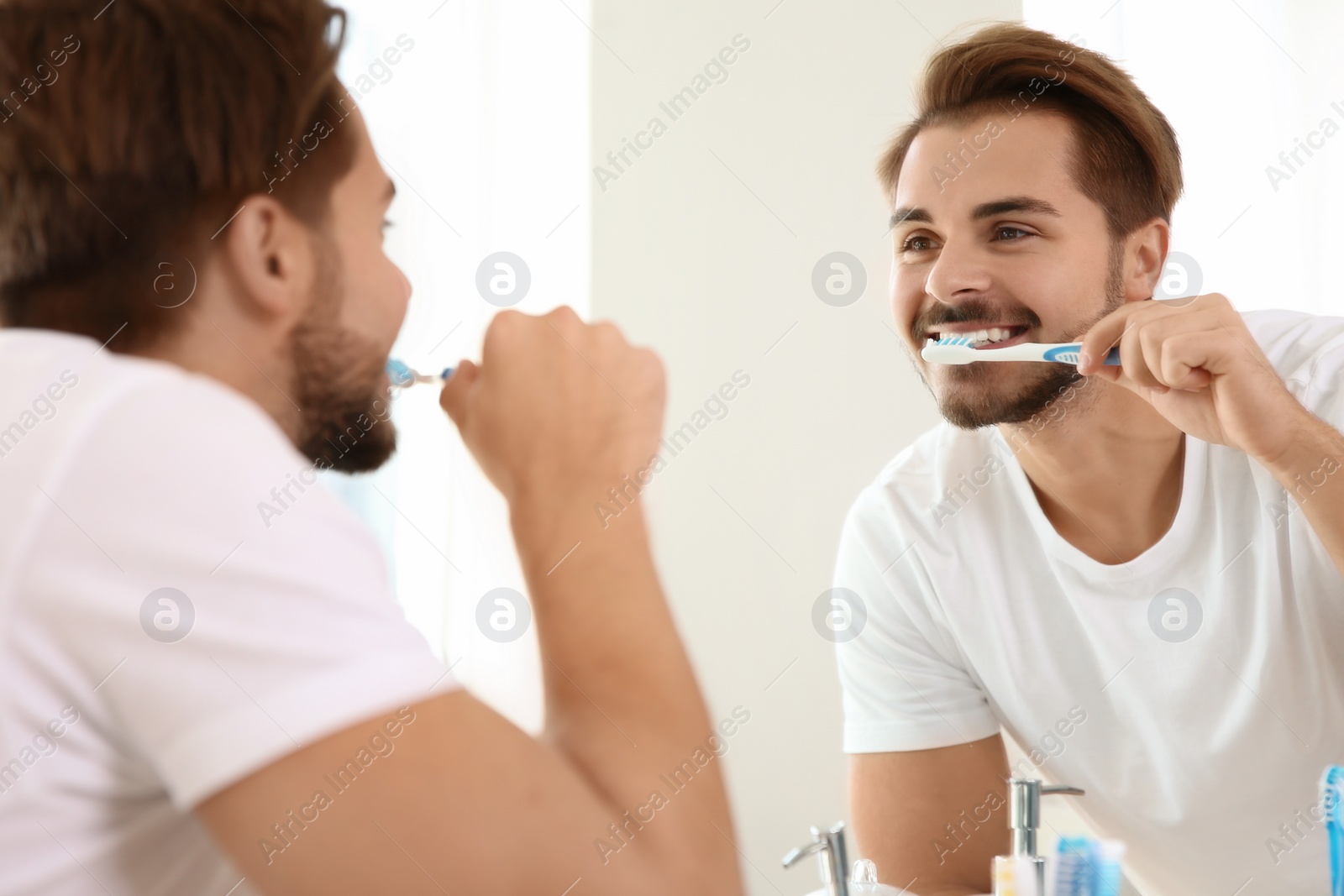 Photo of Young man with toothbrush near mirror in bathroom. Personal hygiene