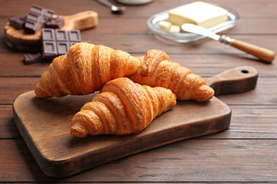 Photo of Board with tasty croissants on wooden table. French pastry