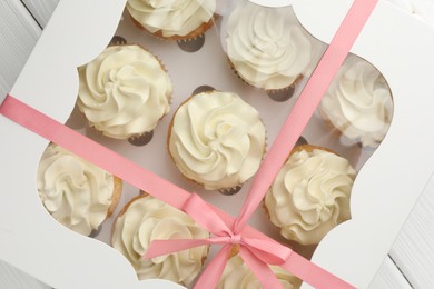 Photo of Tasty cupcakes with vanilla cream in box on white wooden table, top view